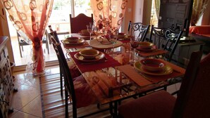 A dining area with a glass table set for four, chairs, and a view of the outdoors through sheer curtains. - Villa with private pool in a quiet location with mountain views 5 min from Ceret (reynes)