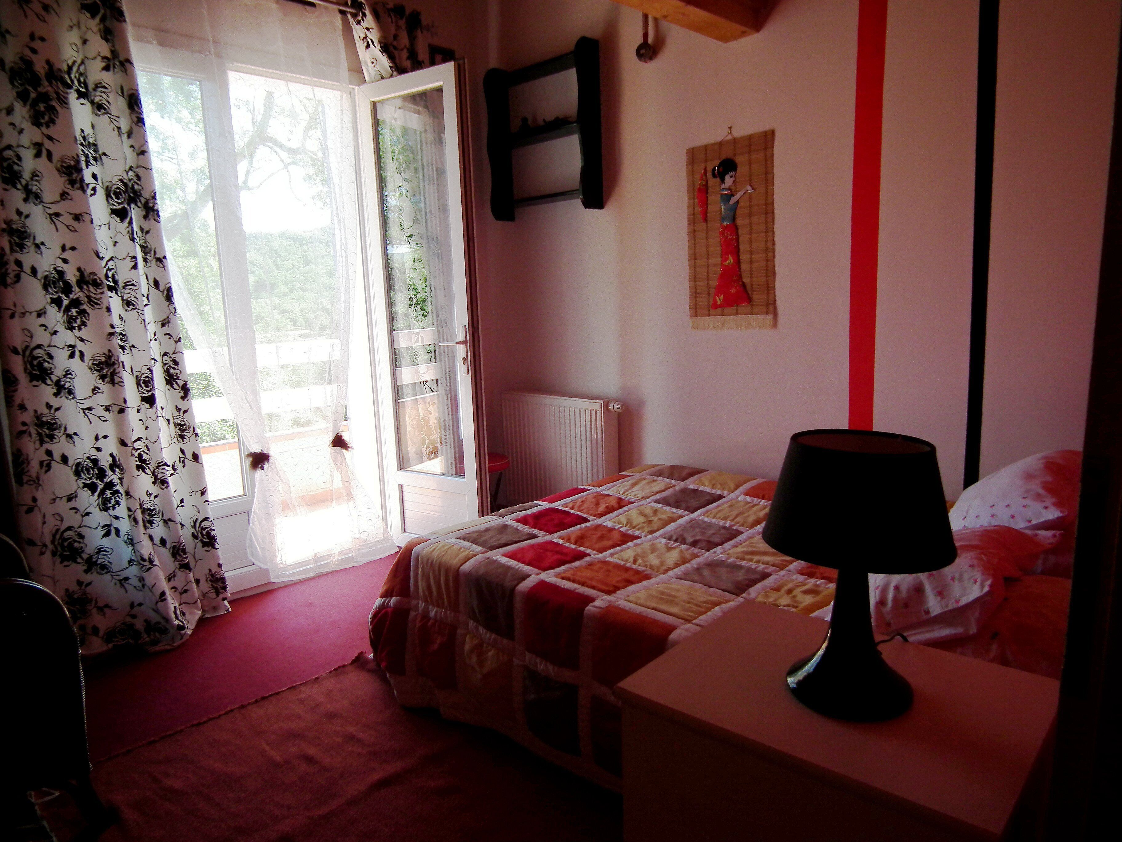 Ein Schlafzimmer mit Bett, Nachttisch, Lampe, einem Fenster mit Vorhängen und einer Heizung.