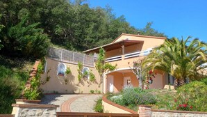 A two-story building with a stone pathway leading to the entrance, surrounded by lush greenery and a clear blue sky. - Villa with private pool in a quiet location with mountain views 5 min from Ceret (reynes)