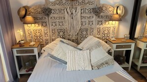 A room with a bed, two nightstands, a decorative headboard, and a wall with intricate patterns.