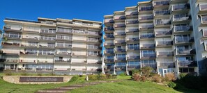 A multi-story residential building with balconies, a sign reading 'L'artantrone,' and a well-maintained lawn.