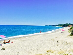 Una playa con agua azul cristalina y una orilla arenosa. Se ven gente y sombrillas.
