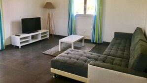 Een woonkamer met een bank, een televisie op een dressoir, een lamp en gordijnen.