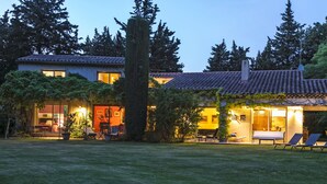 Una casa de dos pisos con tejado de tejas, un árbol grande al frente y un césped bien cuidado.