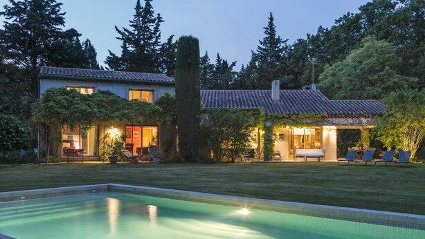 Una propiedad residencial con piscina, un patio con sillones de descanso y un jardín cuidado.