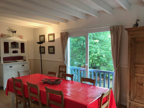 A dining area with a red table and chairs, a white cabinet with glass doors, and a view of greenery through a window.