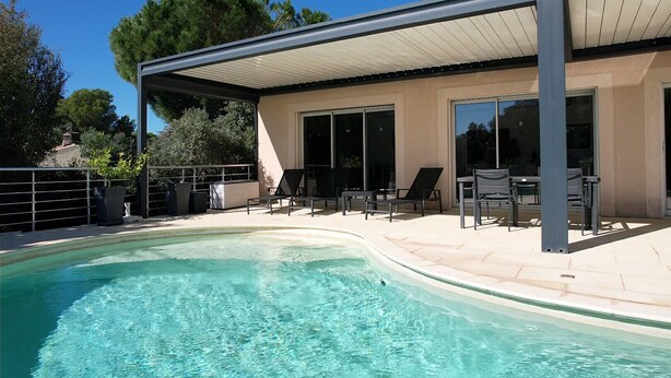 A modern outdoor pool area with a covered patio, lounge chairs, and a clear blue pool.