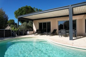 A modern outdoor pool area with a covered patio, lounge chairs, and a clear blue pool. - Vacation rental house with pool AUREILLE LS1-300 (Aureille)