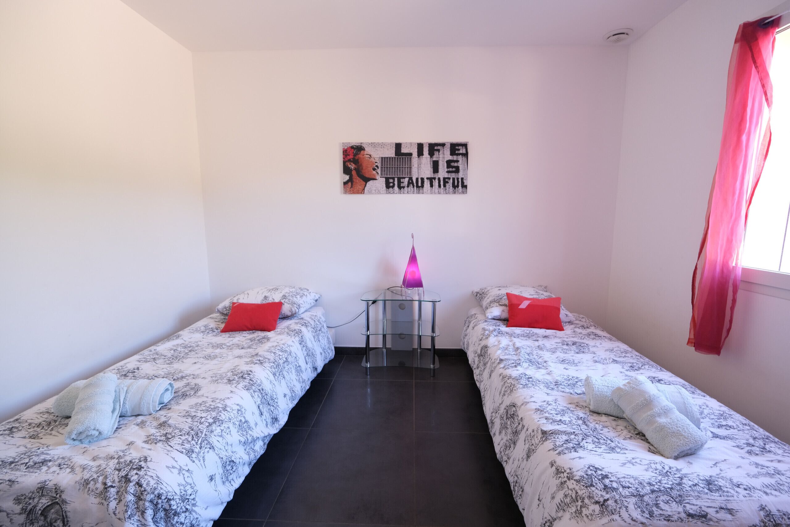 A room with two single beds, a small table with a lamp, and a motivational poster on the wall.