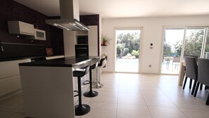 A modern kitchen with a central island, bar stools, a microwave, and a potted plant.
