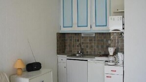 Une cuisine de taille réduite, avec des meubles blancs, un four à micro-ondes, une machine à café et une radio.