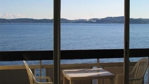 Un balcon donnant sur une étendue d’eau calme et sur des collines lointaines. On y trouve deux chaises et une petite table.