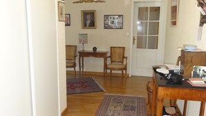 A room with a wooden floor, a patterned rug, a table with a lamp, chairs, and a door. - App. 93m2 bright calm tt comfort, terrace, garage, hyper-center, close station (Annecy)