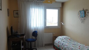 A small, tidy room with a bed, a desk, a chair, a window with curtains, a radiator, and a wall decoration. - App. 93m2 bright calm tt comfort, terrace, garage, hyper-center, close station (Annecy)