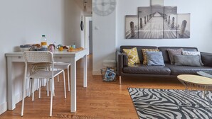 Ein modernes Wohnzimmer mit grauem Sofa, einem Essbereich mit weißem Tisch und Stühlen sowie einem großen, abstrakten Gemälde an der Wand.
