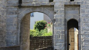 Ein steinerner Bogen mit Holzpfeilung und einem Tor, das zu einem Gebäude mit Fenster und Tür führt.
