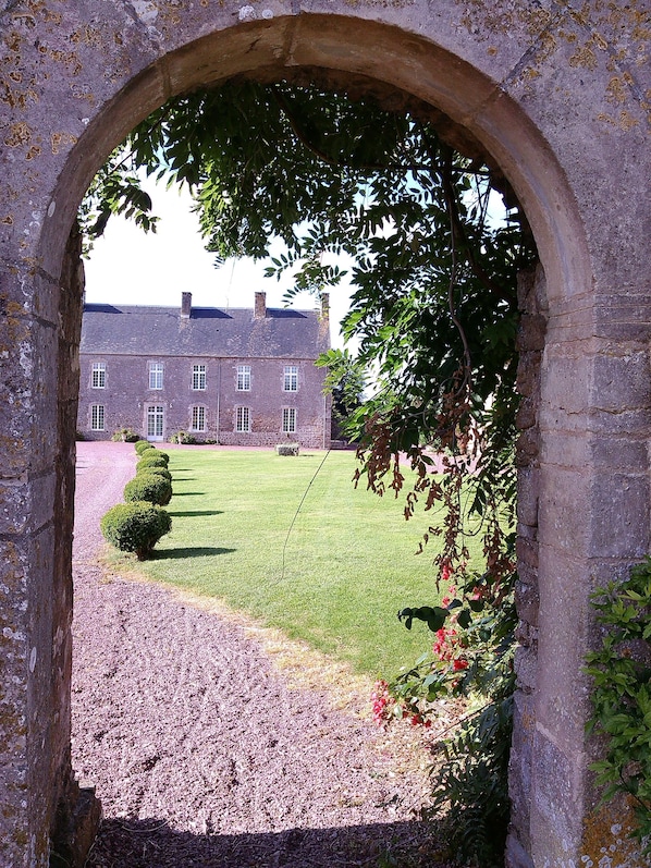 An arched stone doorway leading to a courtyard with a building in the background.