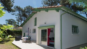 Ein kleines, eingeschossiges Haus mit gefliester Terrasse, einer Schiebetür und einer kleinen Sitzgelegenheit im Freien.