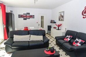 Ein Wohnzimmer mit zwei schwarzen Ledersofas, einem Couchtisch, einem roten Vorhang, einer Küchenzeile und einer weißen Tür.
