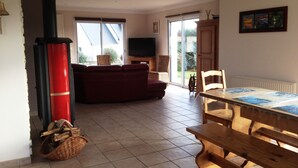 Een woonkamer met een bank, een televisie, een open haard, een eettafel met stoelen en uitzicht op de omgeving.