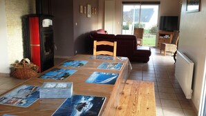 Een eetruimte met een houten tafel, afgedekt met placemats, een rode houtkachel, rieten meubels en uitzicht door een glazen deur.
