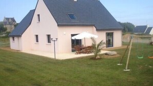 Een gelijkvloers huis met een schuin dak, een terras met tuinmeubilair en een verzorgd gazon.