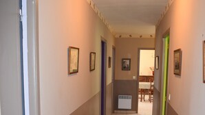 A hallway with a tiled floor, framed pictures on the walls, and a door on the left.