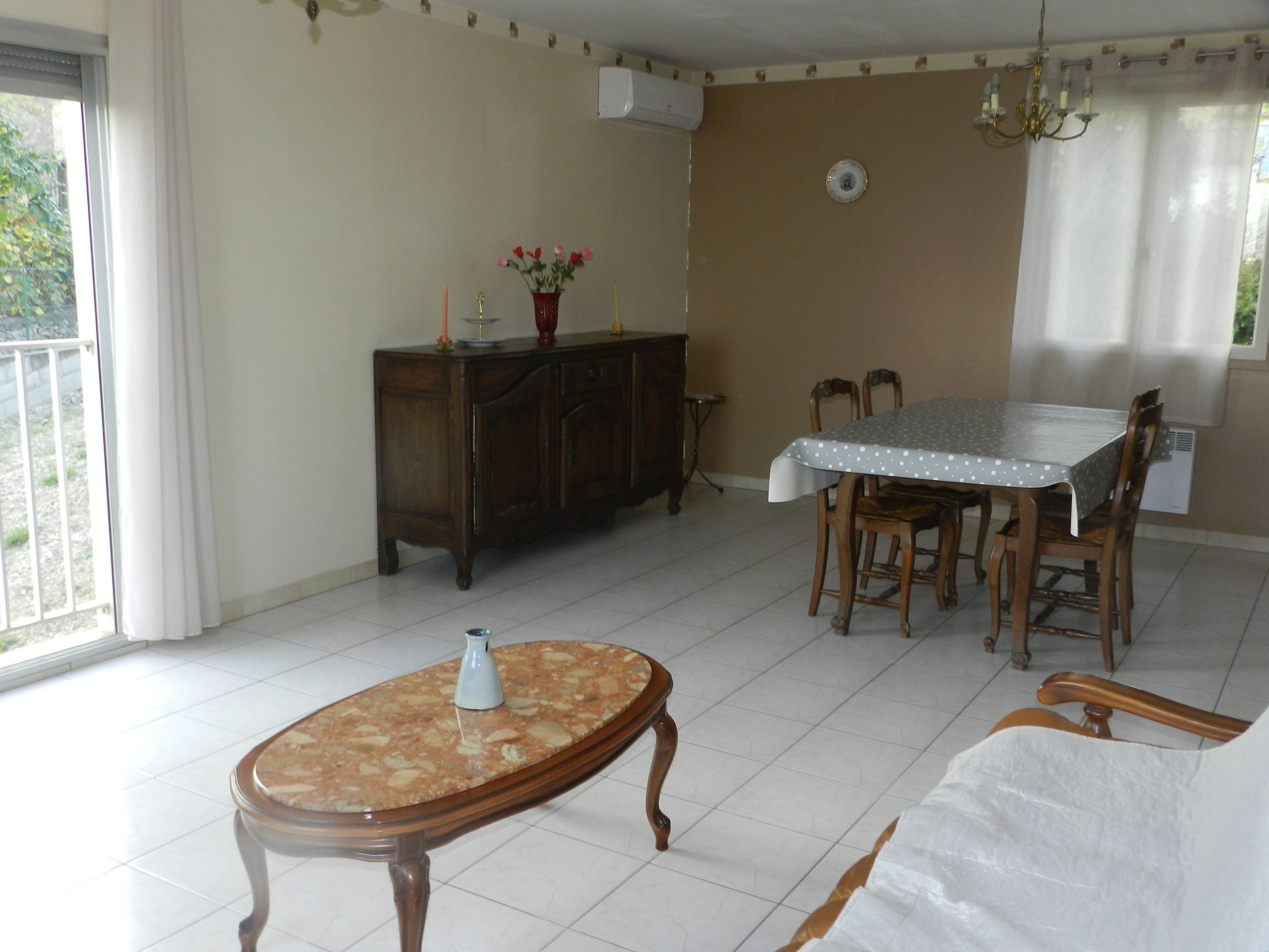 Un comedor con una mesa, sillas, un armario de madera y una mesita con un jarrón.