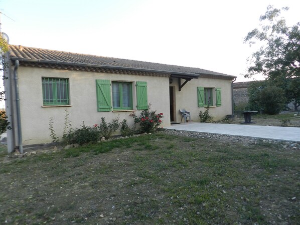 A single-story house with a tiled roof, green shutters, and a small porch area.