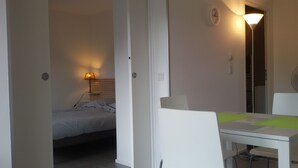 A hotel room with a bed, a bedside table with a lamp, a small table with chairs, and a door leading to a closet.