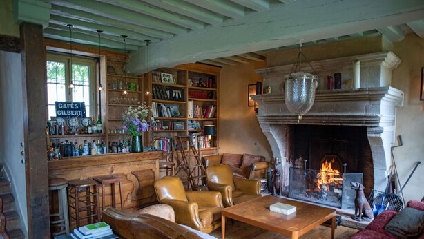 Una sala de estar acogedora con sofás de cuero, una chimenea, una estantería y una zona de bar con diferentes botellas y vasos.