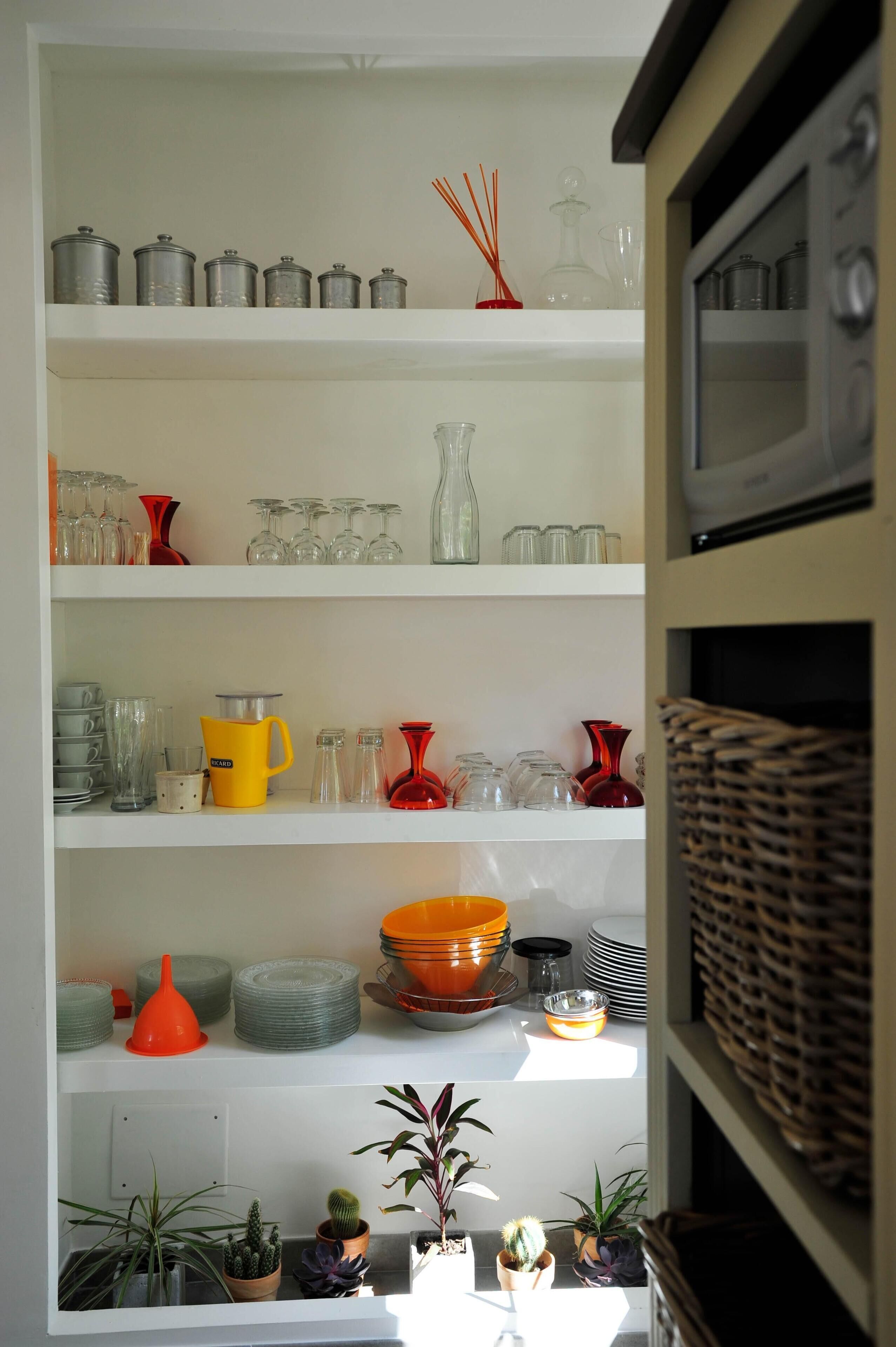 A kitchen with white shelves holding various glassware, a microwave, and potted plants.