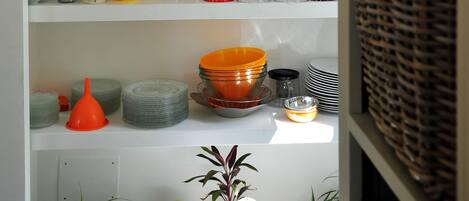 A kitchen with white shelves holding various glassware, a microwave, and potted plants.