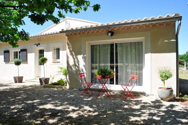 A house with a tiled roof, a large sliding glass door, and a gravel driveway. There are two red chairs and two potted plants near the door. - Brand new house, with all comfort and pool, at the foot of the Mont Ventoux. (Vaison-La-Romaine)