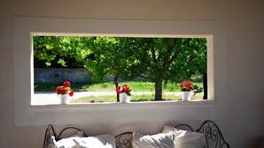 Une chambre avec un lit, des oreillers blancs et une fenêtre ornée de trois pots de fleurs rouges.