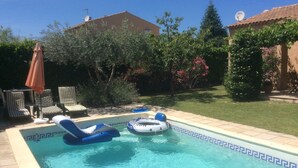 Una piscina con sillas de descanso y flotadores, rodeada de un jardín y una casa.