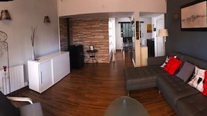 A modern living room with a grey sofa, a small table, and a coffee table. There is a kitchen area in the background with a white fridge and a stove.
