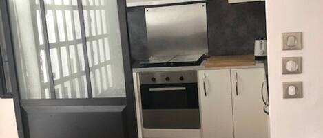 A modern kitchen with a stainless steel range hood, white cabinets, and a black-framed sliding door.