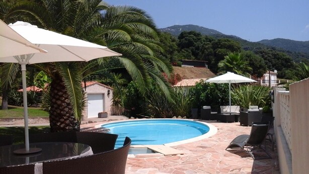 A swimming pool with surrounding patio furniture and umbrellas, set against a backdrop of lush greenery and mountains. - Corsica, self-contained studio, private pool and garden, Ajaccio region (Santa-Maria-Siché)