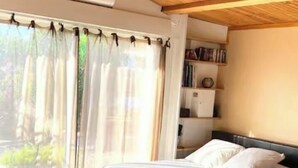 A bedroom with a bed, a bedside table, a bookshelf, and a window with curtains. - Corsica, self-contained studio, private pool and garden, Ajaccio region (Santa-Maria-Siché)
