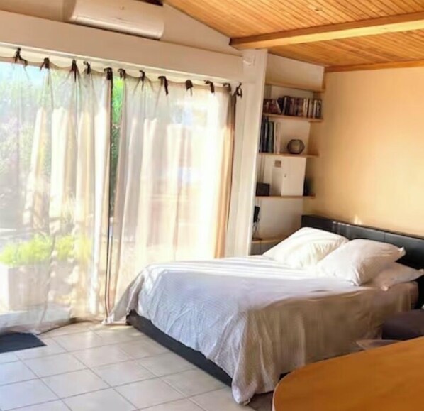 A bedroom with a bed, a bedside table, a bookshelf, and a window with curtains.