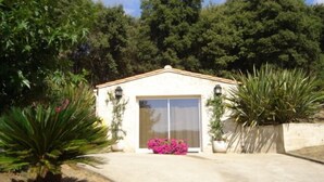 A small, single-story building with a white exterior and a sloped roof. It features a large sliding glass door and two wall-mounted lanterns. - Corsica, self-contained studio, private pool and garden, Ajaccio region (Santa-Maria-Siché)