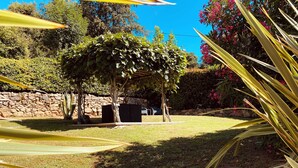 A covered outdoor seating area with a stone wall and greenery in the background. - Corsica, self-contained studio, private pool and garden, Ajaccio region (Santa-Maria-Siché)