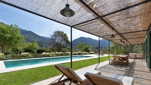 Un espacio exterior techado con piscina, sillas de descanso y una mesa.