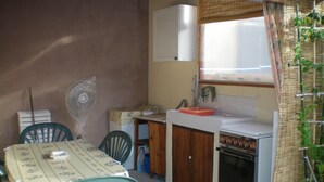 Et kompakt køkken med vask, komfur og ventilator. Der er et bord med stole og et vindue med gardiner.