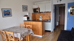 A compact kitchen with a wooden island, a dining table with chairs, and a black sofa in the living area.