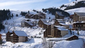 A snow-covered mountain resort with multiple chalet-style buildings, ski slopes, and a clear sky.