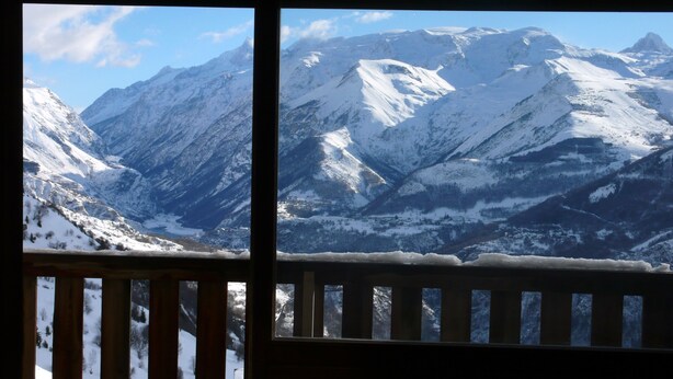 A mountain landscape with snow-covered peaks and a wooden railing in the foreground.