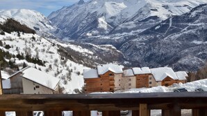 A mountain lodge with multiple wooden buildings, snow-covered roofs, and a backdrop of snow-capped mountains.