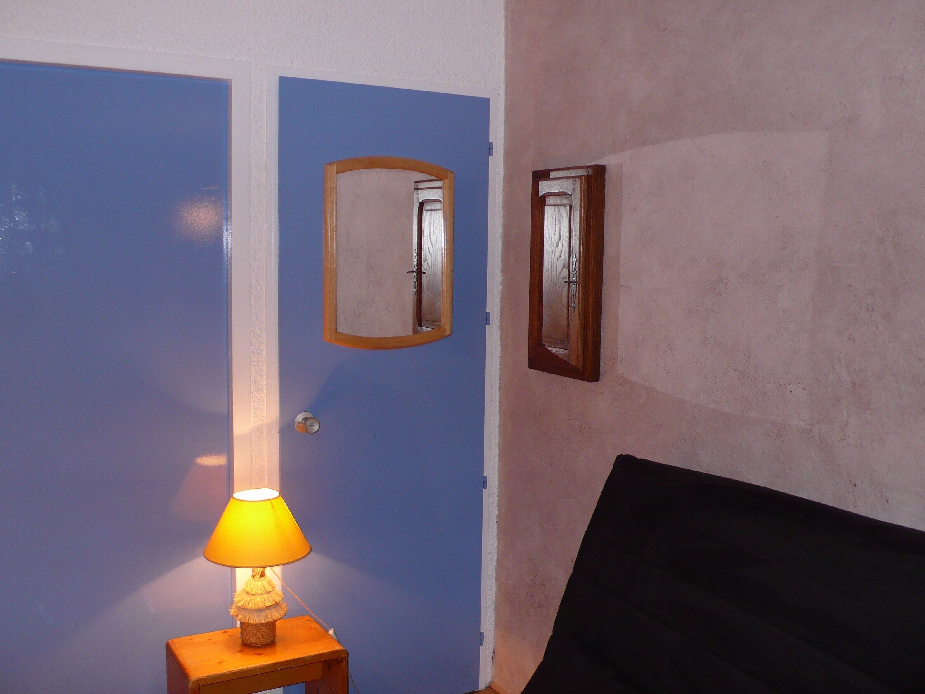 Una stanza con una porta blu, un tavolino con una lampada e un letto con testiera nera.
